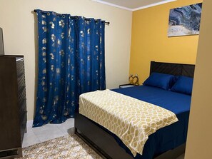 A bedroom with a bed, curtains, a painting, and a dresser. - Escape into our spacious suite designed for ultimate relaxation in Montego Bay. (Montego Bay)