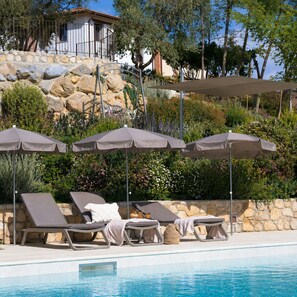 A poolside area with lounge chairs and umbrellas, a stone wall, and a building in the background.