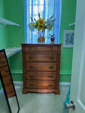 Quarto com paredes verdes, penteadeira de madeira com várias gavetas, janela com cortinas azuis e porta com puxador azul-turquesa.