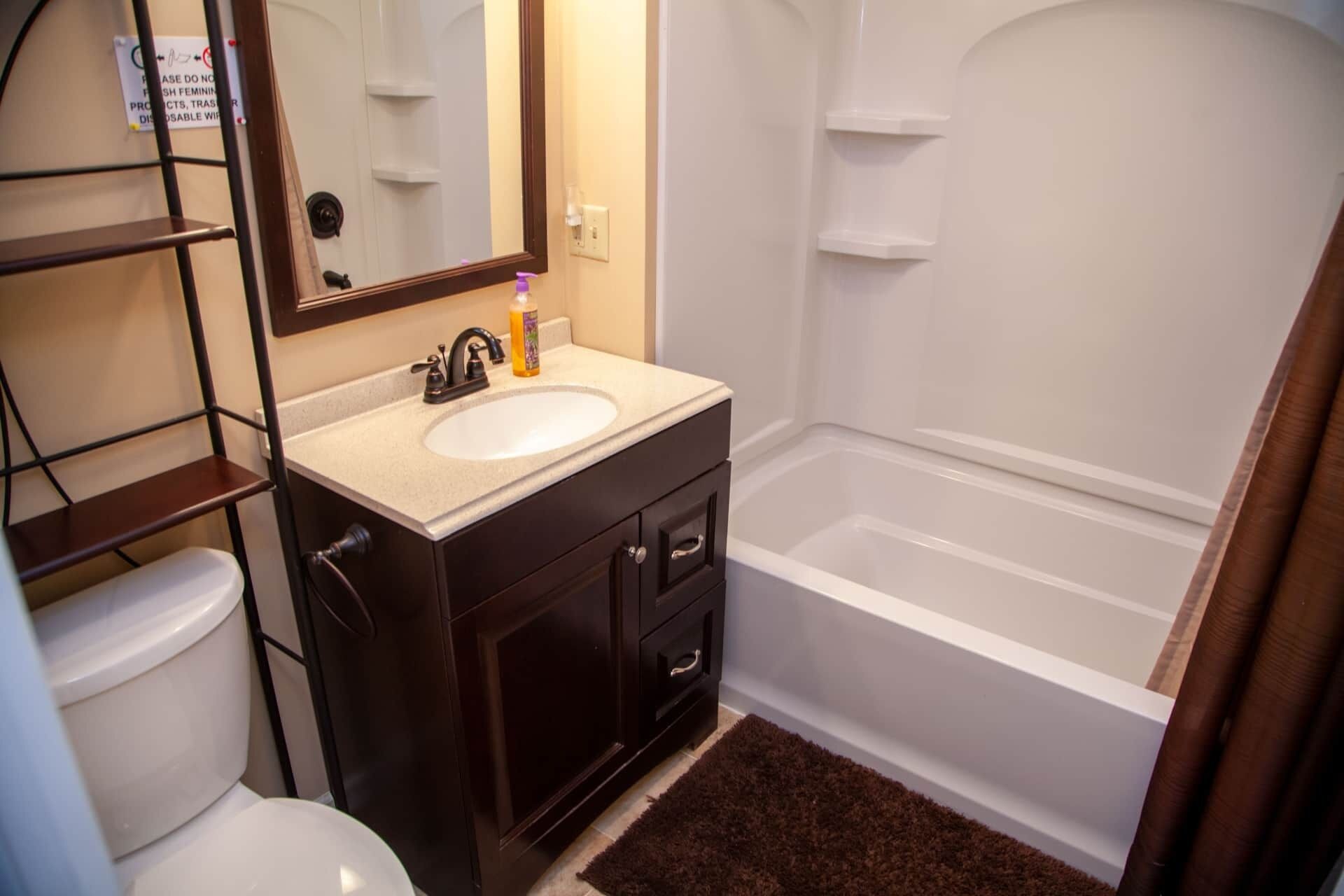 Une salle de bain avec un lavabo blanc, un meuble-lavabo en bois foncé, un miroir, des toilettes et une baignoire.