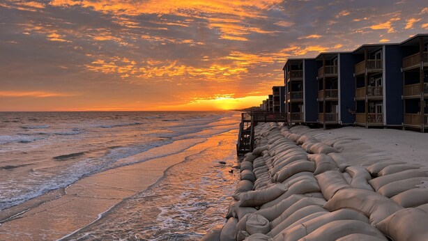 Un hôtel situé en bord de mer, doté de nombreux balcons, d’une plage de sable et offrant une vue imprenable sur le coucher de soleil.