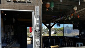 Un coin bar rustique en bois, agrémenté d’une enseigne indiquant « TIKI » et d’une décoration en forme de visage sculpté dans le bois.