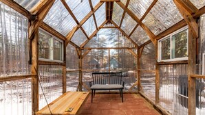 A greenhouse with a wooden bench and table, large windows, and a view of a snowy landscape. - River Access, hot tub, dogs! (Conway)