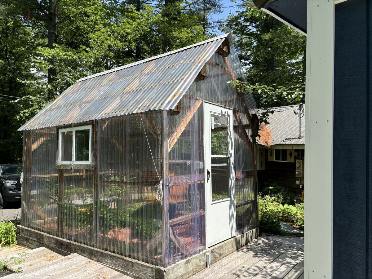 A small, single-story greenhouse with a corrugated metal roof and a door.