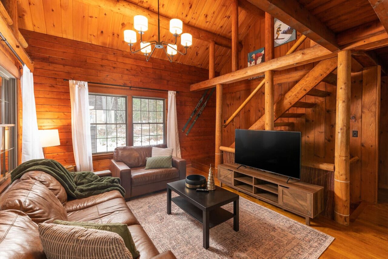 Ein gemütliches Blockhaus-Interieur mit Sofa, Fernseher und einer Holztreppe.