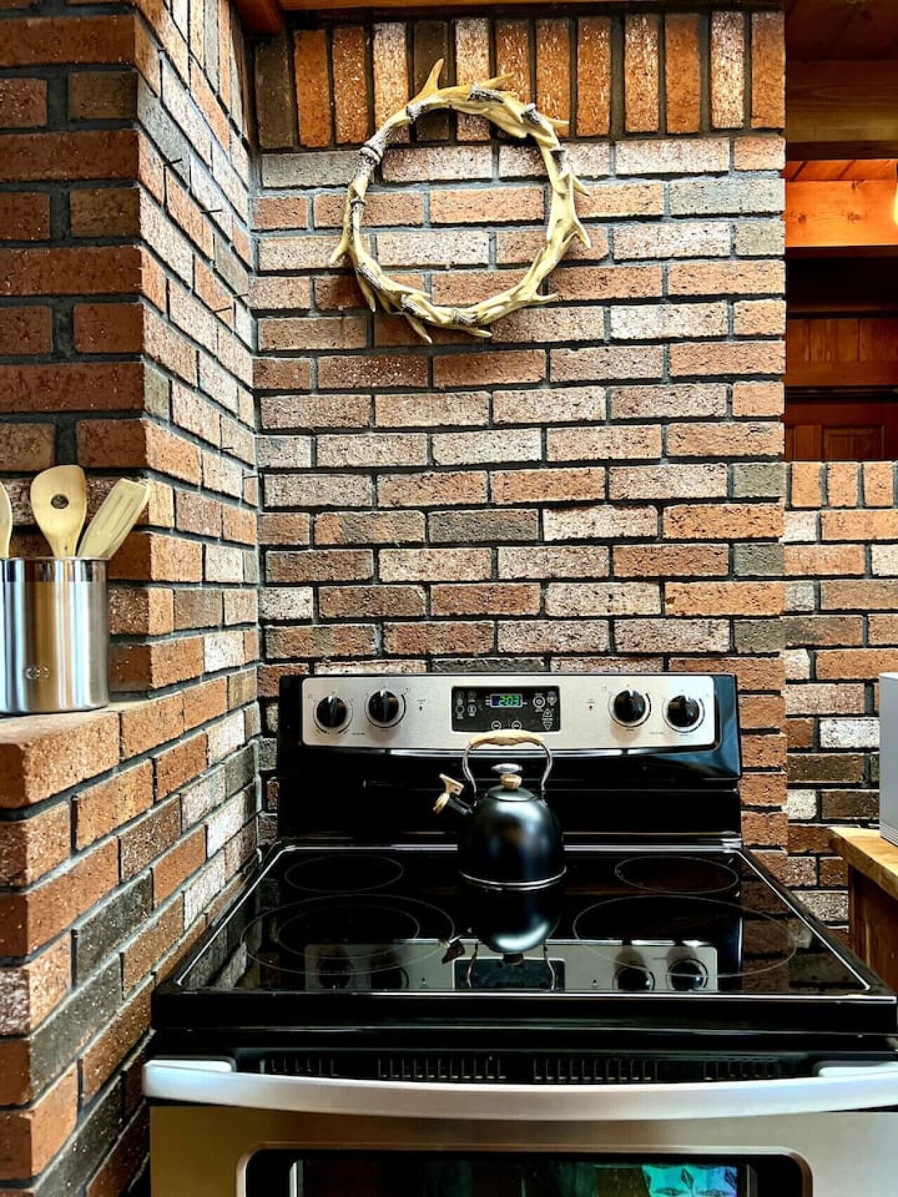 A kitchen with a brick wall, a stove, and a kettle.