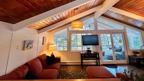 Een gezellige loft-living met houten plafond, groot raam, flatscreen-tv en rode bank.