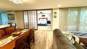 Uma sala ampla com uma mesa de jantar, um sofá e uma porta deslizante que dá para um quarto.
