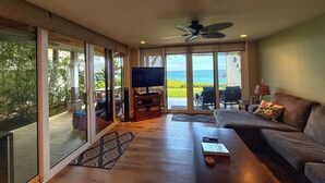 Sala de estar com televisão, sofá e vista para o oceano através de amplas portas de correr de vidro.
