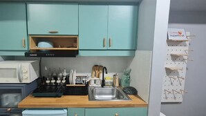 A compact kitchen with teal cabinets, a microwave, a stove, and a sink. There are utensils and bottles on the counter.