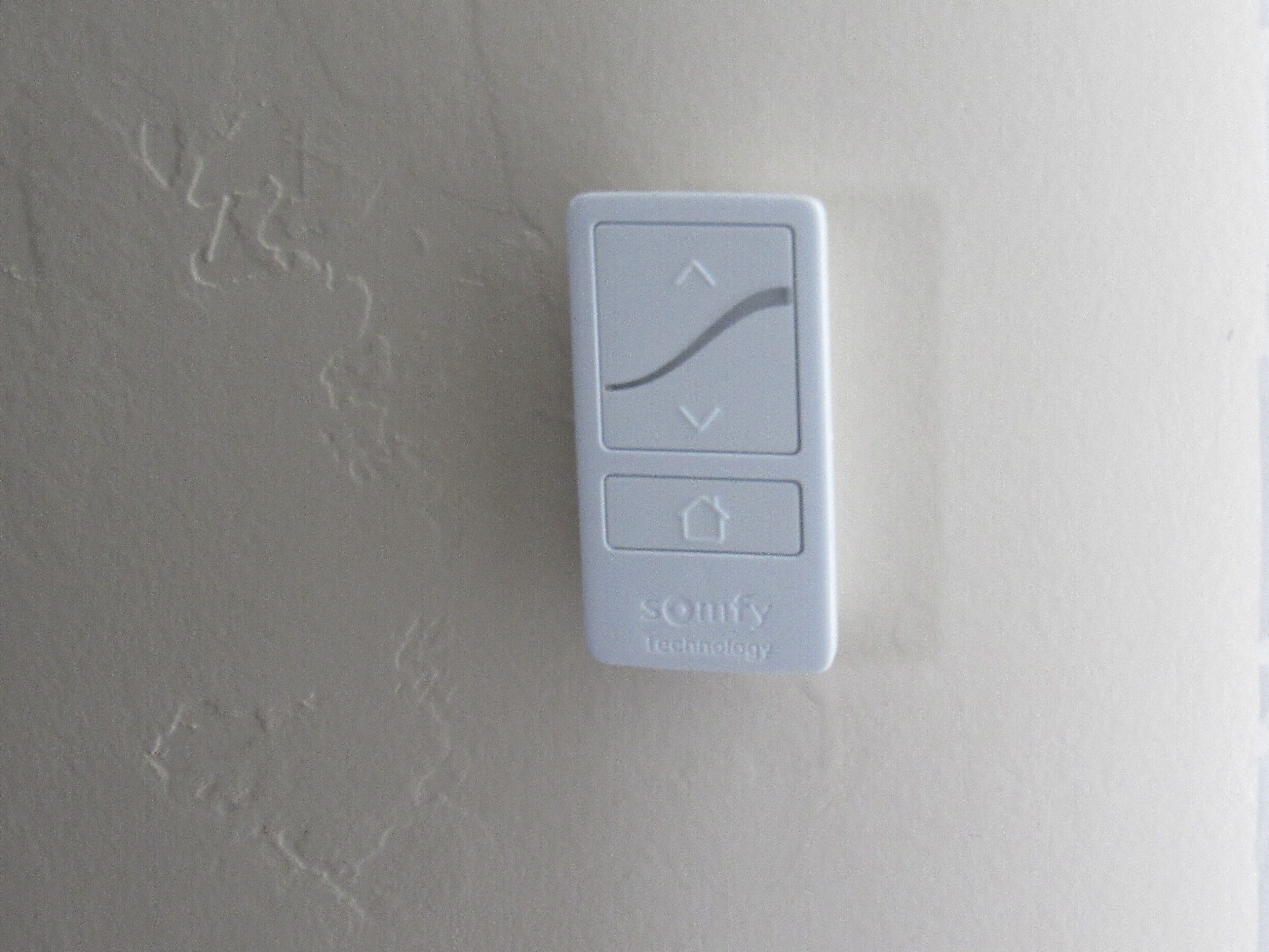 A thermostat with a rising temperature indicator and a house icon, mounted on a textured wall.