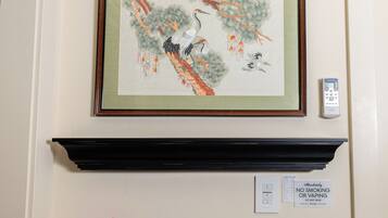 Un climatiseur fixé au mur, un tableau encadré, une télécommande, un panneau indiquant qu’il est interdit de fumer et un pot d’orchidée.