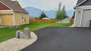 Un camino de acceso residencial con superficie pavimentada, borde de grava y valla de madera.
