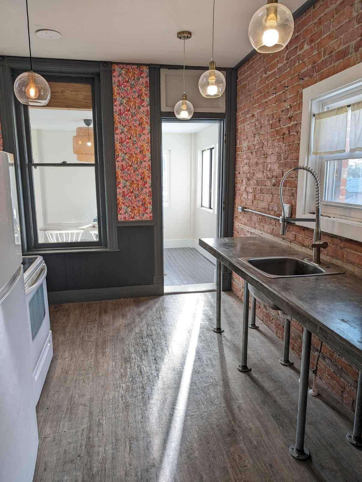 A kitchen with a brick wall, a stainless steel sink, and pendant lights.