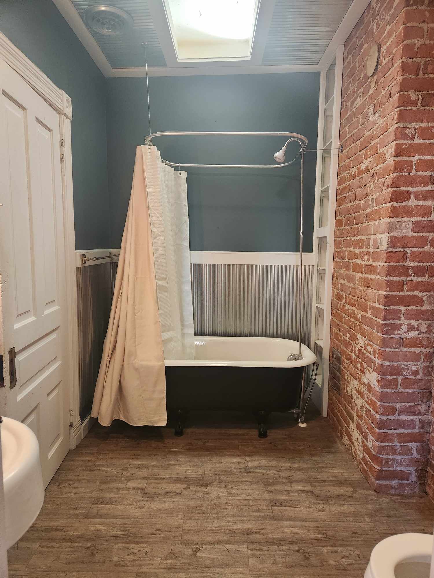 Et lille, aflangt badeværelse med ovenlys, badekar, toilet og en murstensvæg.