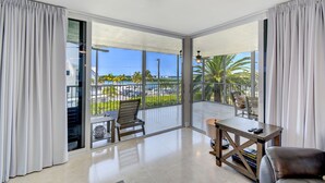 A spacious balcony with a view of the ocean and palm trees, furnished with a table, chairs, and a sofa.