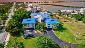 A coastal hotel with a central building featuring a blue roof, surrounded by lush greenery and a marina.