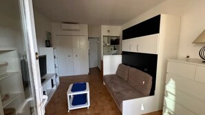 Ein kompakter Wohnbereich mit Küchenzeile, einer Couch, einem kleinen Tisch und einem Fernseher.