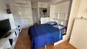 Ein Schlafzimmer mit Bett, Fernseher, Kleiderschrank und einer kleinen Küchenzeile.