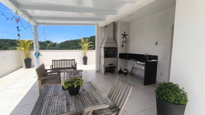 An outdoor patio with a table and chairs, a grill, and potted plants. - Refúgio Praiano (Bombinhas)