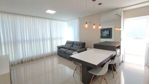 A modern living room with a sofa, a dining table, and a TV. - Refúgio Praiano (Bombinhas)