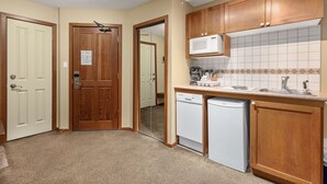 A compact kitchen with wooden cabinets, a microwave, a dishwasher, and a tiled backsplash. - Cascade Lodge suite ski/bike storage room WIFI pool 2 hot tub sauna gym cable TV (Whistler)