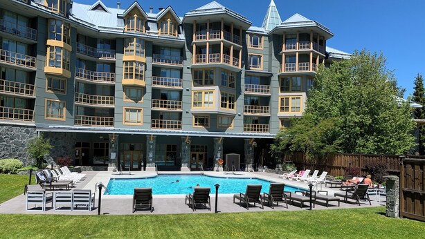 A multi-story hotel with a swimming pool, outdoor seating, and a stone facade. - Cascade Lodge suite ski/bike storage room WIFI pool 2 hot tub sauna gym cable TV (Whistler)