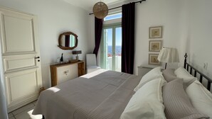 A bedroom with a bed, dresser, and a large window with curtains. - Waterfront Villa with private swimming pool-walking distance to a sandy cove. (Kea)