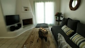 A living room with a flat-screen TV, a fireplace, a wooden coffee table, and a dark-colored sofa with striped pillows. - Waterfront Villa with private swimming pool-walking distance to a sandy cove. (Kea)