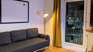 Un salón con un sofá gris, una lámpara de pie y un ventanal corredero con cortinas.