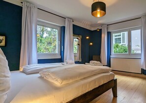 A bedroom with a large bed, two windows with curtains, a radiator, and a hanging light fixture.