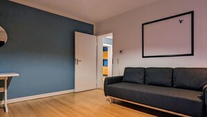 Una habitación con una pared azul oscuro, suelo de madera, sofá negro, puerta blanca y un cuadro enmarcado en la pared.