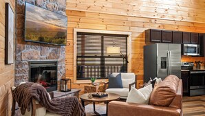 A cozy living room with a stone fireplace, a comfortable sofa, a coffee table, and a modern kitchen area.