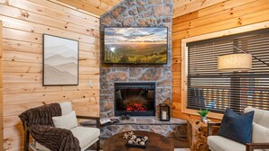 A cozy living room with a stone fireplace, wooden walls, and a comfortable seating area.