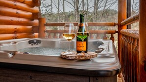 A hot tub with a bottle of wine and a glass on a wooden platform.