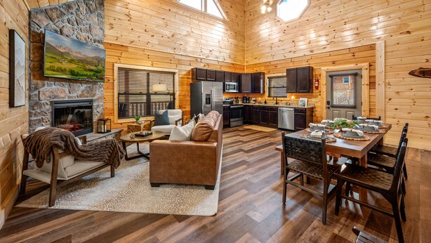 A spacious cabin with a fireplace, a cozy seating area, a dining table set for six, and a kitchen with dark cabinets.