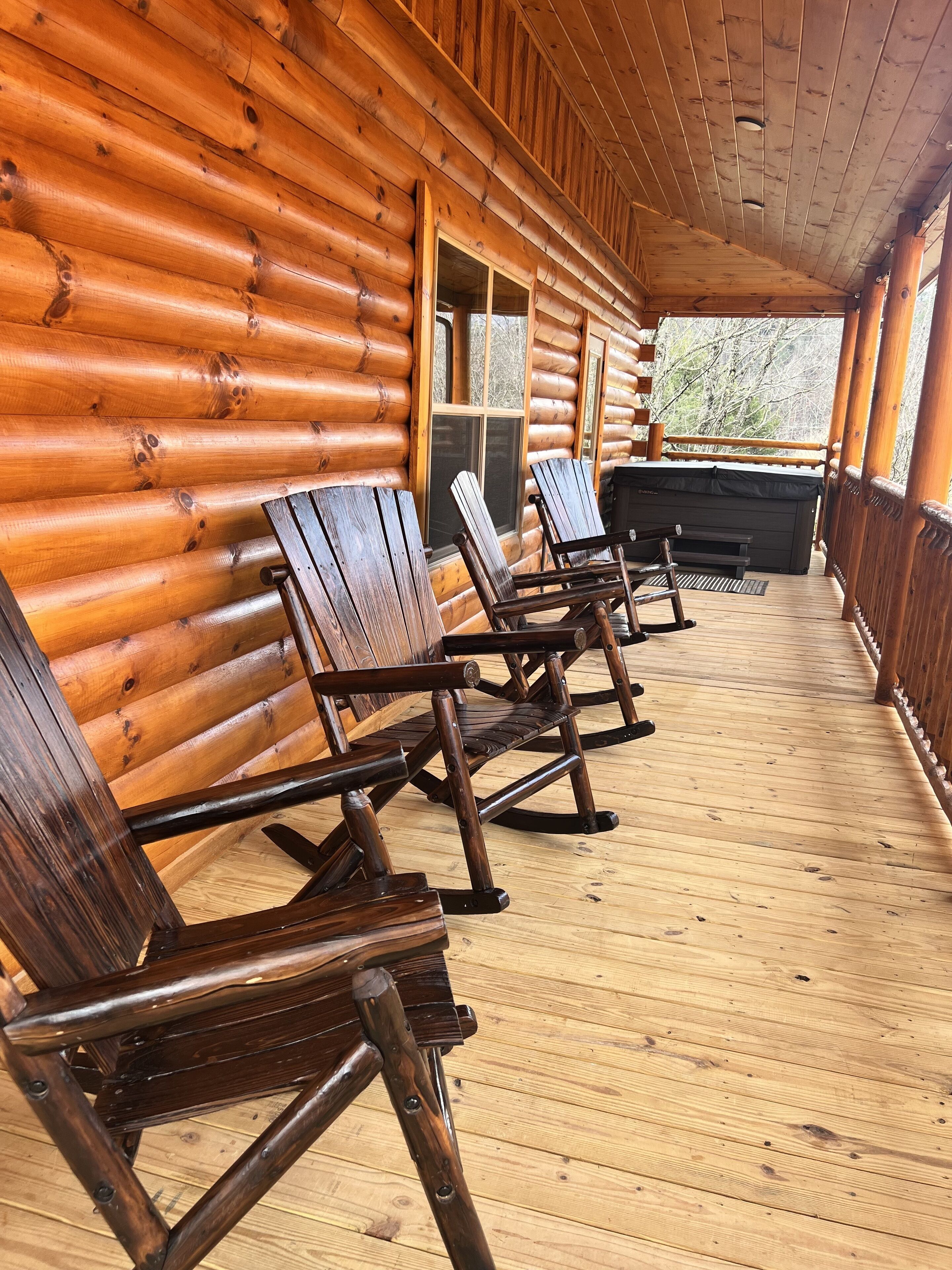 Eine Blockhütte mit Veranda, auf der Schaukelstühle und ein Whirlpool stehen.