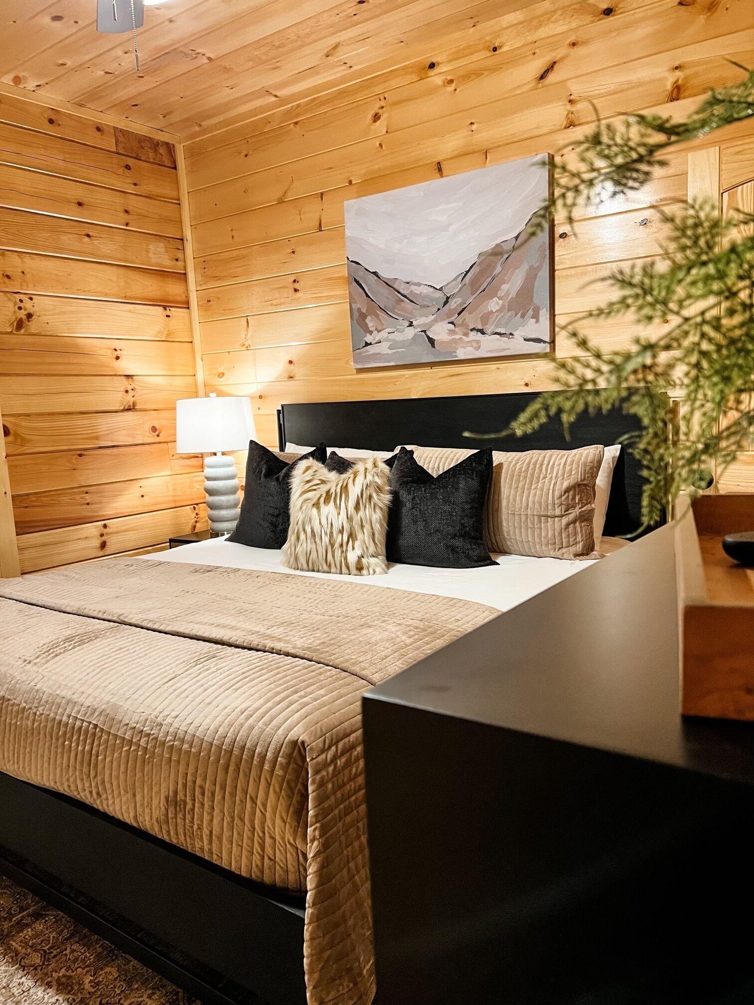 A wooden cabin-style bedroom with a bed, a nightstand, a lamp, and a painting on the wall.