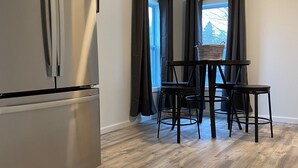 A modern kitchen with a stainless steel refrigerator, a dining table with chairs, and a window with curtains. - Cozy Country home just 5 miles to Boyne City/8 miles to Boyne Mountain (Boyne City)