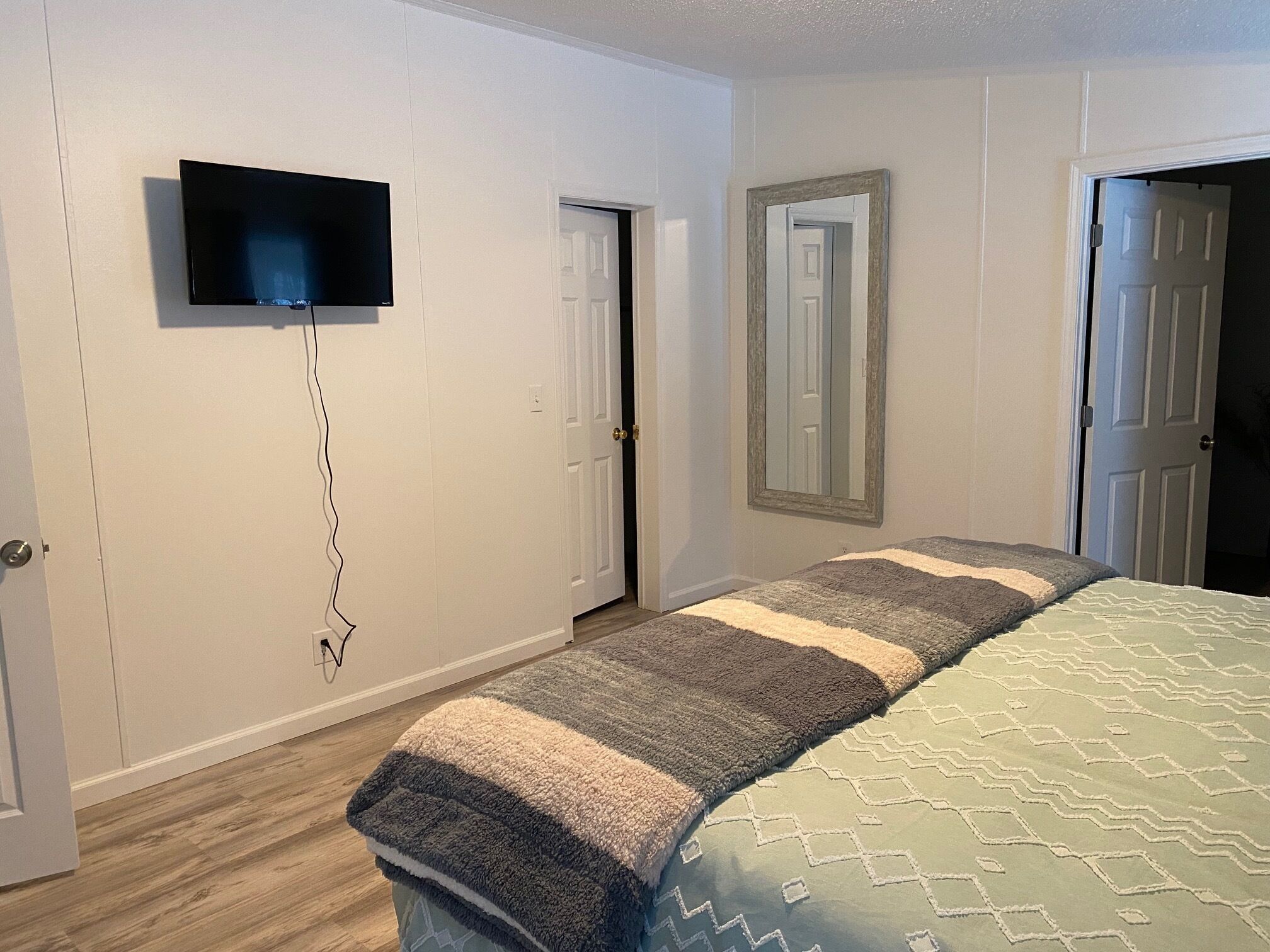 Een slaapkamer met een bed, een aan de muur bevestigde televisie en twee deuren.