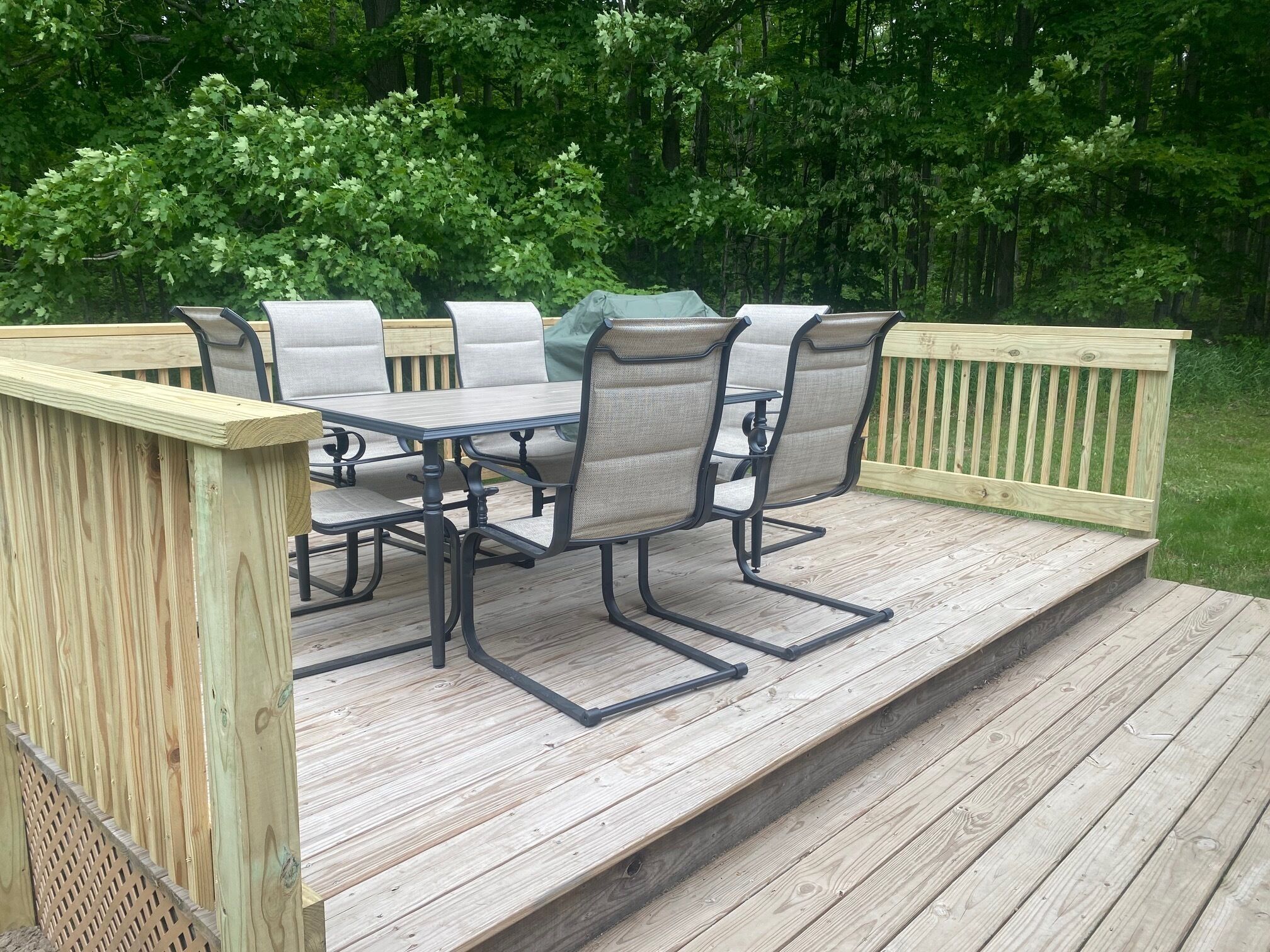 A wooden deck with a table and chairs, surrounded by a wooden railing and a wooden fence.