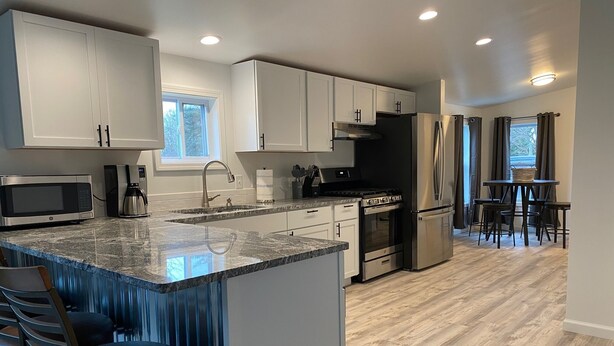 A modern kitchen with white cabinets, a granite countertop, stainless steel appliances, and a bar area with stools. - Cozy Country home just 5 miles to Boyne City/8 miles to Boyne Mountain (Boyne City)