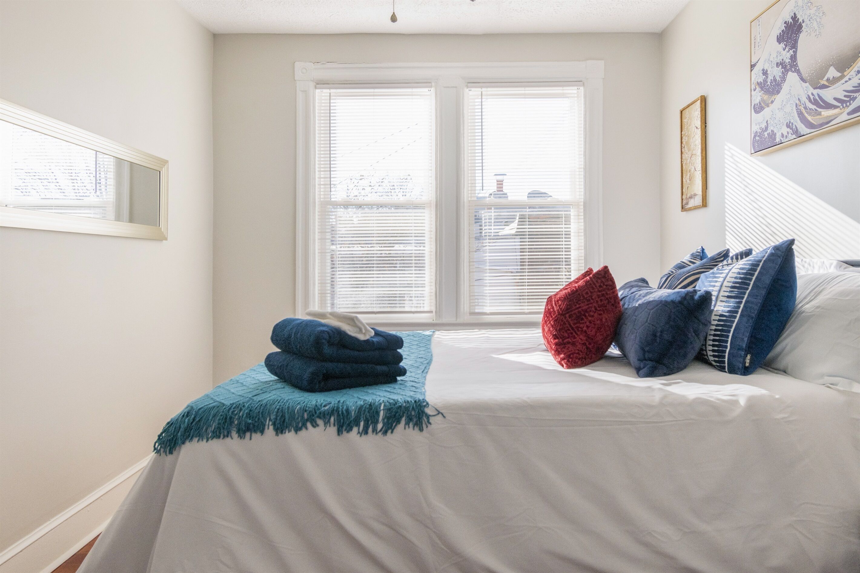 Een slaapkamer met een bed, een raam met zonwering en een schilderij aan de muur.