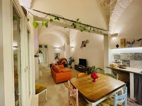 A cozy living room with a wooden dining table, orange sofa, and a TV. - At the Palazzotto (Fasano)