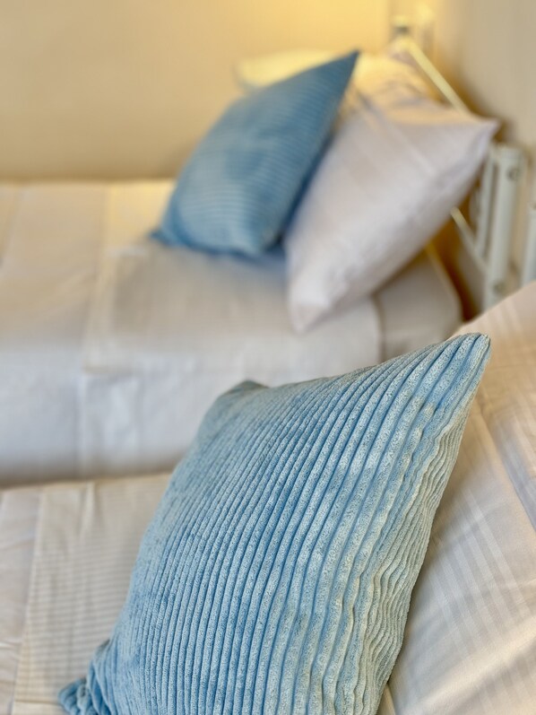 Cama com roupa de cama branca e duas almofadas, uma azul e outra branca.
