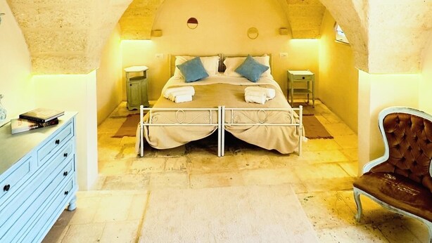 Une chambre à coucher avec une arche en pierre, un lit double avec des oreillers, des tables de chevet, une commode et une chaise.