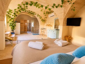 A bedroom with a bed, a dresser, a television, and a bathroom visible through an archway. - At the Palazzotto (Fasano)