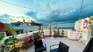 Une terrasse sur le toit agrémentée de plantes en pot, de meubles d’extérieur et de guirlandes lumineuses.