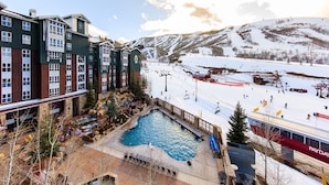 A hotel with a pool, ski slopes, and a mountain backdrop.
