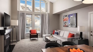 A modern living room with a sofa, armchair, and dining table. There is a television, a lamp, and a painting on the wall.